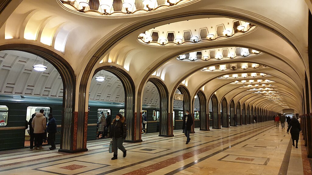 Unutrašnjost moskovske metro stanice sa raskošnim lusterima i mermernim lukovima.