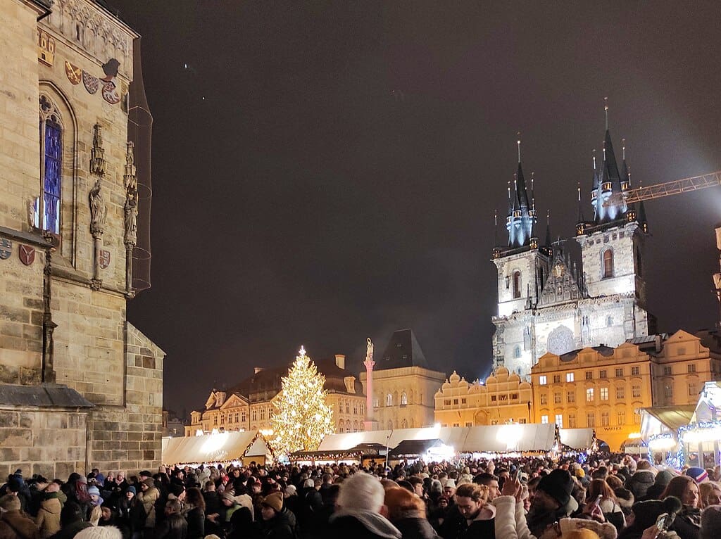 Praznična scena na Starom gradskom trgu u Pragu, sa kućicama, svjetlima i istorijskim kulisama.